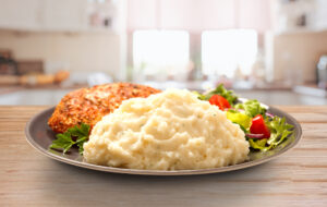 Idahoan Chicken Broth Mashed Potatoes with chicken and salad on a kitchen counter.